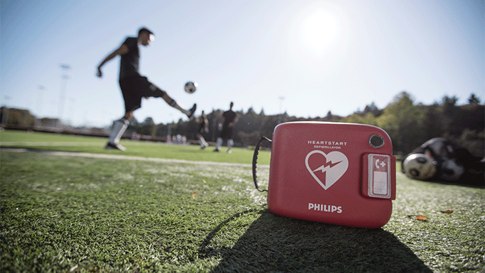 Un botiqu&iacute;n de primeros auxilios rojo sobre el c&eacute;sped con un jugador de f&uacute;tbol pateando una pelota.